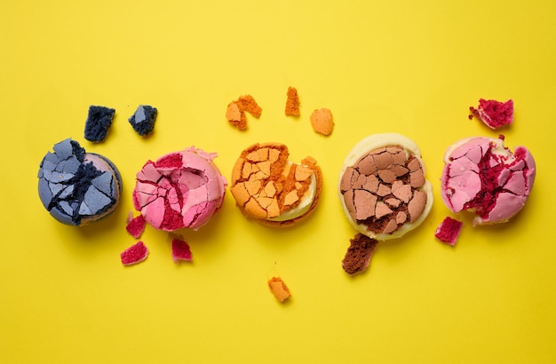 Broken round macarons with crumbs on a yellow background, delicious dessert, top view