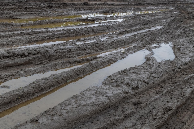 A broken rural country road after the rain puddles after rain\
on a dirt road clay soil and puddles at cloudy day light after rain\
autumn season