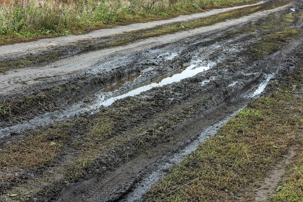 A broken rural country road after the rain puddles on a dirt\
road clay soil and puddles at cloudy day light after rain autumn\
season