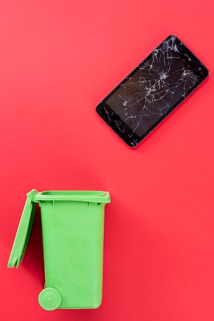 Broken screen mobile phone and green trash can. Recycling.