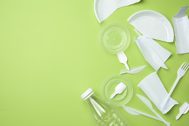 Broken white plastic tableware, transparent bottle on green