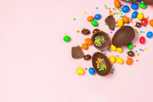 Broken and whole chocolate Easter eggs, multicolored sweets, pink background. Shrub. Concept of celebrating Easter, Easter decorations. Flat lay, top view. Copy Space. Happy Easter.