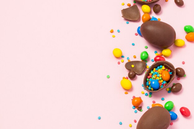 Uova di pasqua di cioccolato rotte e intere, dolci multicolori, sfondo rosa. arbusto. concetto di celebrare la pasqua, decorazioni pasquali. vista piana, vista dall'alto. copia spazio. buona pasqua.