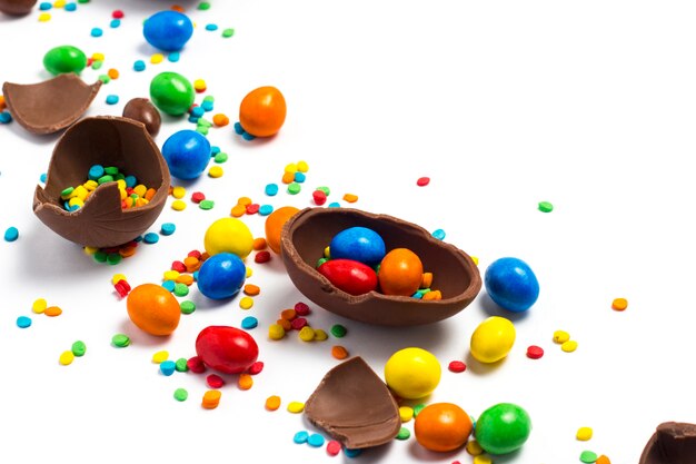 Broken and whole chocolate Easter eggs, multicolored sweets on white. Concept of celebrating Easter, Easter decorations, search for sweets for Easter Bunny. Flat lay, top view. Copy Space.