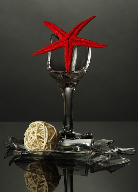 Broken wineglass with sea star on grey background