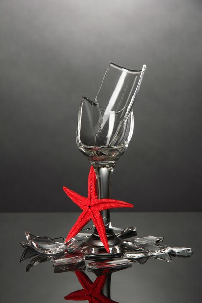 Broken wineglass with sea star on grey background