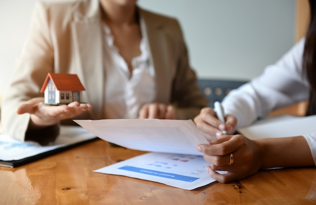 Brokers home sales are working on the table.She holds pen and house model in hand.