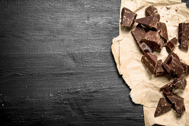 Foto brokken chocolade op oud papier op het zwarte bord