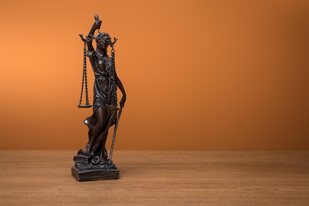 Bronze statuette with scales of justice on wooden table on orange background