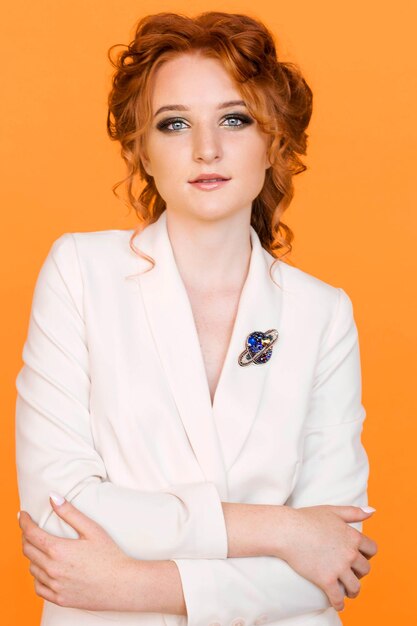 Brooch in the shape of a planet with a ring on the white jacket of a redhaired girl Girl posing on orange background