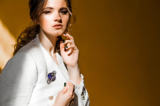 Brooch in the shape of a planet with a ring on a young woman's white jacket light from the sun makes a shadow on a yellow background