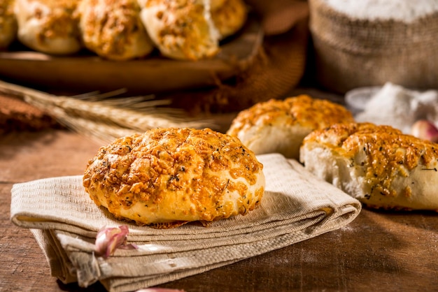 Brood gemaakt met knoflook op doek op rustieke houten tafel met ander brood, knoflook en bloem op de achtergrond.