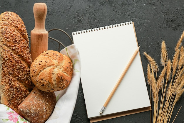 Brood in een mand op een zwarte ondergrond. Geassorteerde brood in een metalen mand. Plaats voor recept en tekst. Bak brood met een deegroller en bloem. Roggebrood, boekweitbroodjes en stokbrood met zaden.