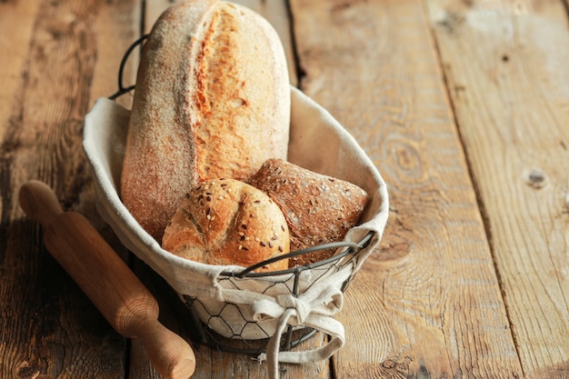 Brood in een mand op een zwarte ondergrond. Geassorteerde brood in een metalen mand. Plaats voor recept en tekst. Bak brood met een deegroller en bloem. Roggebrood, boekweitbroodjes en stokbrood met zaden.