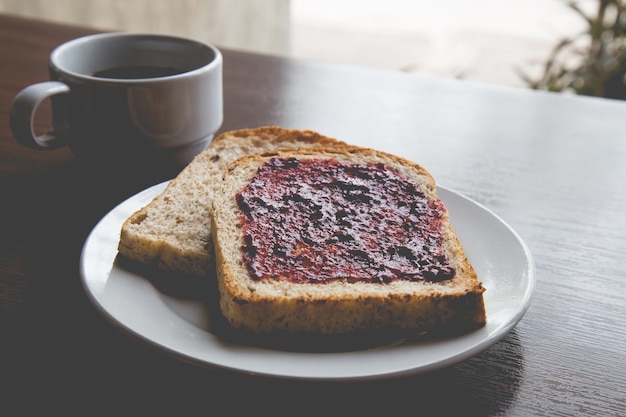 Brood met aardbeienjam en warme koffie op een houten tafel.