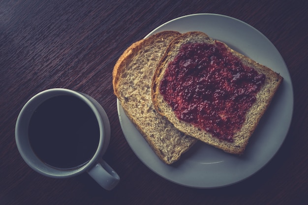 Brood met aardbeienjam en warme koffie op een houten tafel.