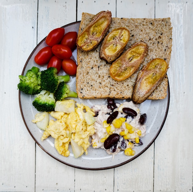 Brood met gebakken bananen roerei met uien rode bonen cherrytomaatjes en broccoli op een schotel