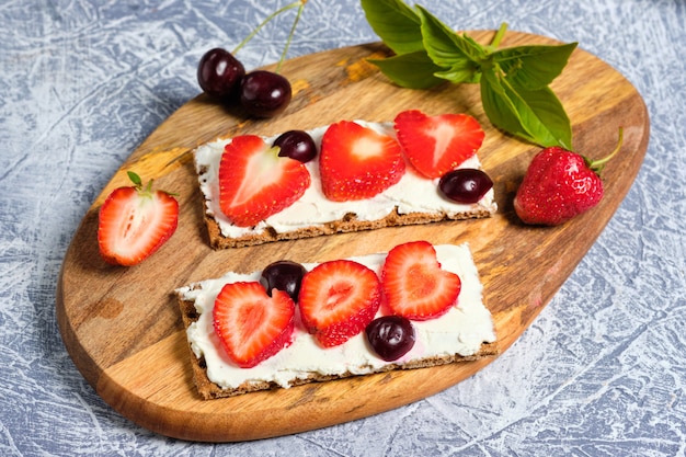 Foto brood met kwark, verse aardbeien en kersen op een houten bord