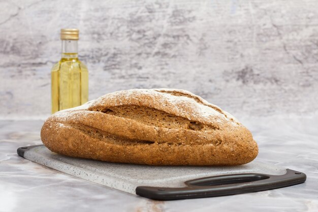 Brood van roggebrood op een snijplank en een fles zonnebloemolie met de grijze achtergrond.