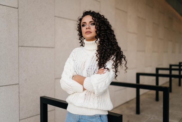 Brooding look and arms crossed on her chest by a curly brunette against the background of the wall