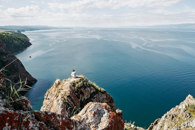 Foto l'uomo meditabondo si siede sul bordo della roccia davanti allo spazio di mare aperto, vista dall'alto