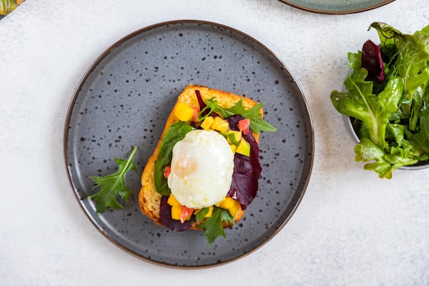 Broodje brioche met gepocheerd ei met zalm en avocado en mangosalsa met rucola en salade