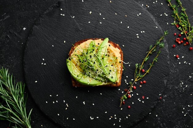 Broodje: ciabatta, avocado, hummus en microgroen. Ontbijt. Op een zwarte stenen plaat.