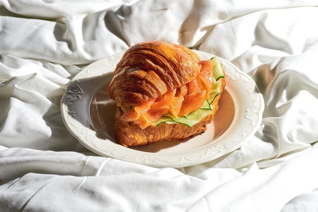 Broodje croissant met zalm en komkommer in een bord op een wit laken Stoer licht