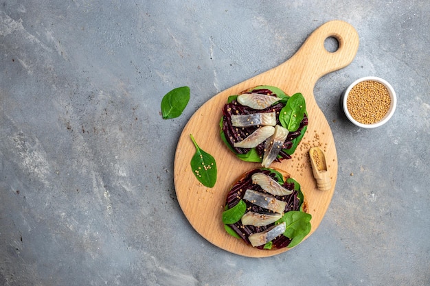 Broodje haringfilet met plakjes ingelegde Atlantische haringfilet rode biet salade groene spinazie ui op een houten bord Scandinavische keuken bovenaanzicht