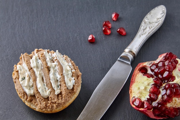 Broodje huisgemaakte paté en saus belegd op toast en granaatappelpitjes, op zwarte stenen plank