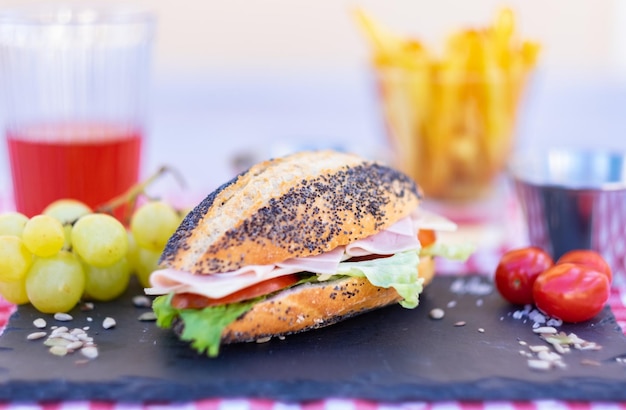 Broodje maanzaad met groenten en gekookte ham op een zwarte stenen snijplank Lichte en gezonde snack Frietjes en een glas wijn op de achtergrond