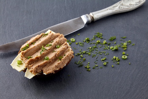 Broodje met huisgemaakte paté belegd op brood en boter, gegarneerd met dille op een zwarte leisteen plank