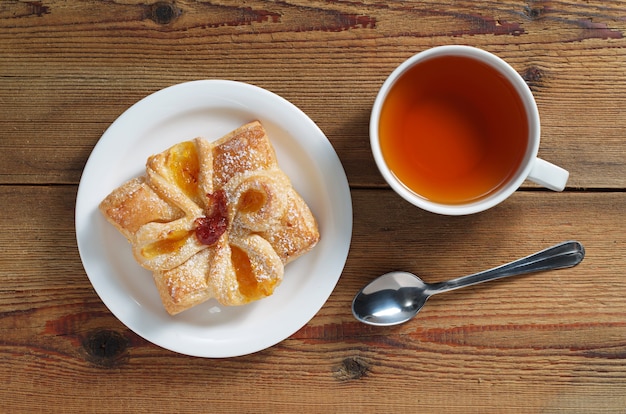 Broodje met jam en kopje thee op een houten tafel