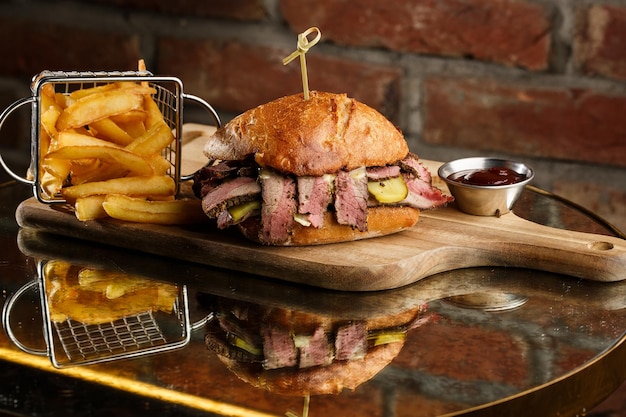 Broodje Pastrami op roggebrood geserveerd met augurk en mosterdsaus Lekkere sandwich met frietaardappelen op donkere achtergrond