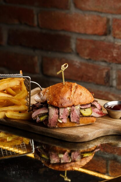 Foto broodje pastrami op roggebrood geserveerd met augurk en mosterdsaus lekkere sandwich met frietaardappelen op donkere achtergrond