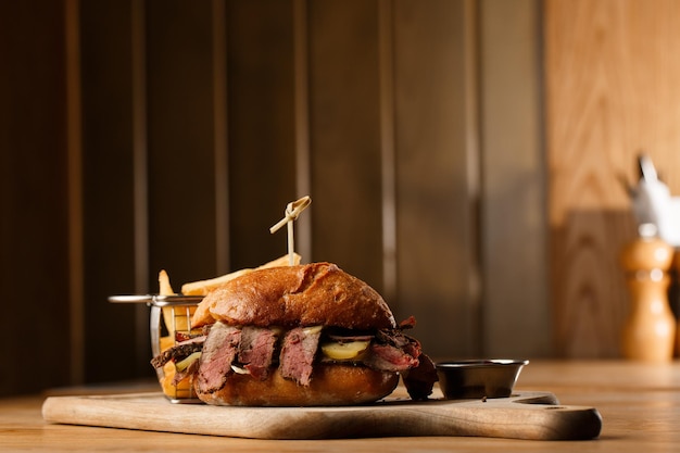 Broodje Pastrami op roggebrood geserveerd met augurk en mosterdsaus Lekkere sandwich met frietaardappelen op donkere achtergrond