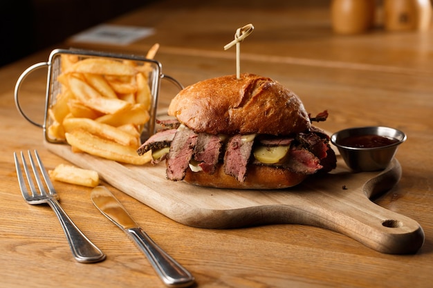 Broodje Pastrami op roggebrood geserveerd met augurk en mosterdsaus Lekkere sandwich met frietaardappelen op donkere achtergrond