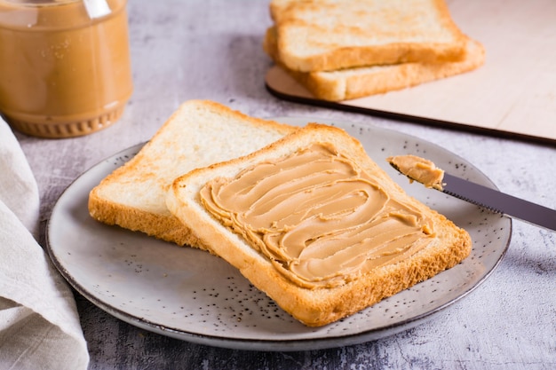 Broodje pindakaas op geroosterd brood op een bord en potje boter op tafel