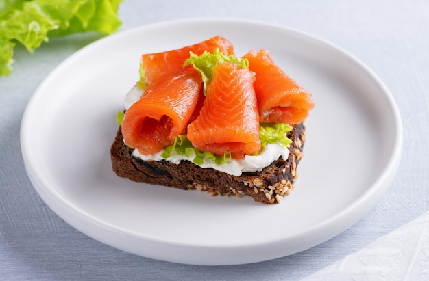 Broodje zalmfilet met roomkaas op een licht houten tafel