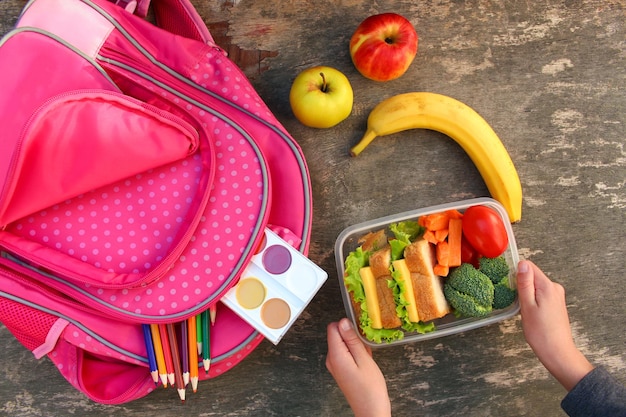 Broodjes, fruit en groenten in voedseldoos, rugzak op oude houten ondergrond. Concept kind dat op school eet. Bovenaanzicht. Plat leggen.