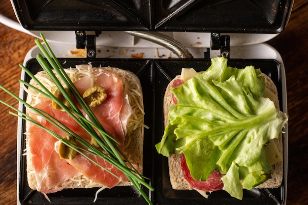 Broodjes maken van ham, groenten en kaas in een tosti-ijzer Twee toastjes met verschillende vullingen close-up