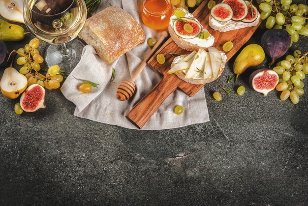 Broodjes met kaas, ciabatta, verse vijgen, peren, druiven, walnoten en honing op een houten bord over donkere grijze stenen tafel