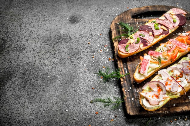 Broodjes met vlees, salami, zeevruchten en verse groenten op rustieke tafel.