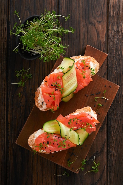 Broodjes Zalm toast met roomkaas komkommer zwarte sesam en microgreens op oude houten tafel achtergrond Zeevruchten gezonde voeding fotografie in low key bovenaanzicht