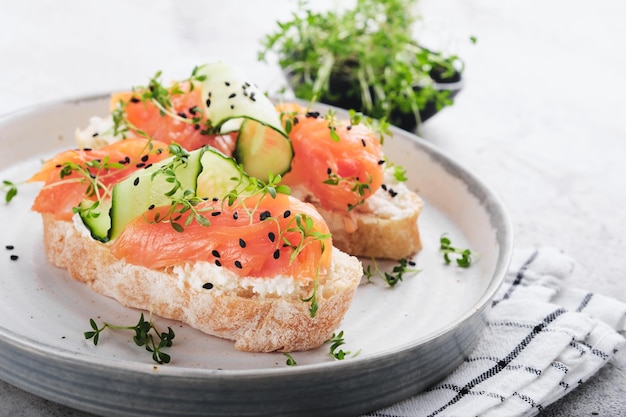 Foto broodjes zalmtoast met roomkaas, komkommer, zwarte sesam en microgreens op grijze betonnen tafelachtergrond zeevruchten gezonde voeding bovenaanzicht