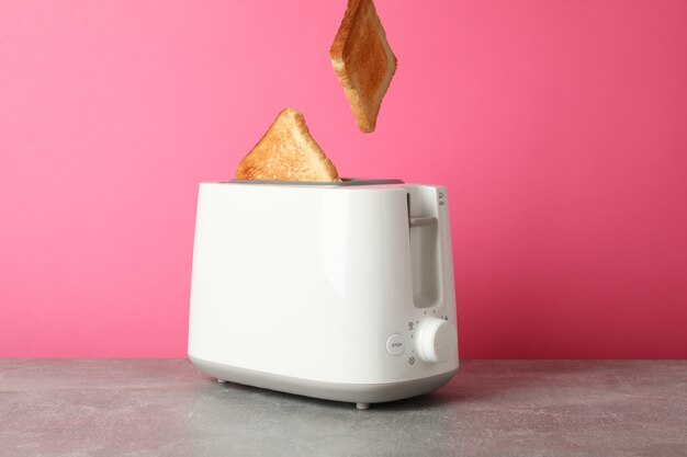 Broodrooster en sneetjes brood op grijze tafel tegen roze achtergrond, ruimte voor tekst