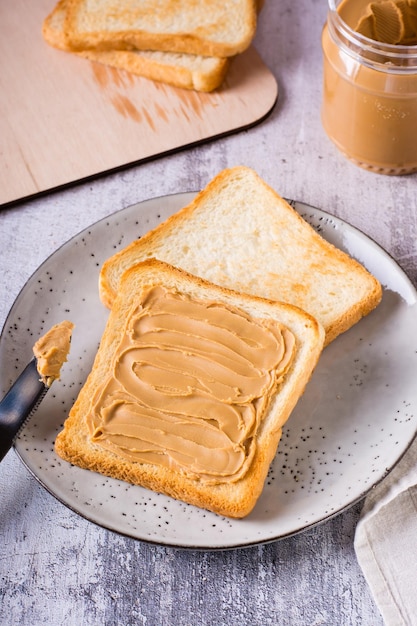 Broodtoast met pindakaas op een bord en een potje boter op tafel Verticaal zicht