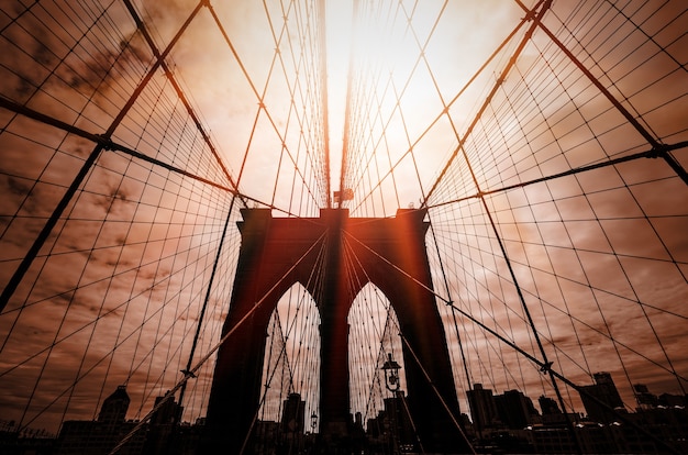 Brooklyn bridge silhouette with a dramatic red sky and sun rays. New York City. USA.