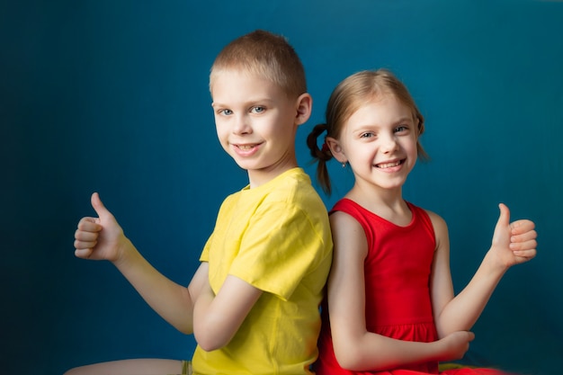 Фото Брат и сестра на синем фоне в яркой одежде показывают