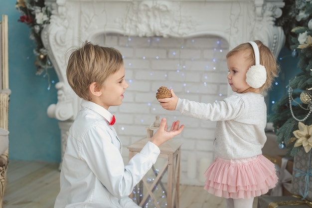 Fratello e sorellina sotto l'albero di natale. ragazzo sorridente che dà il regalo di natale alla ragazza. vacanze in famiglia